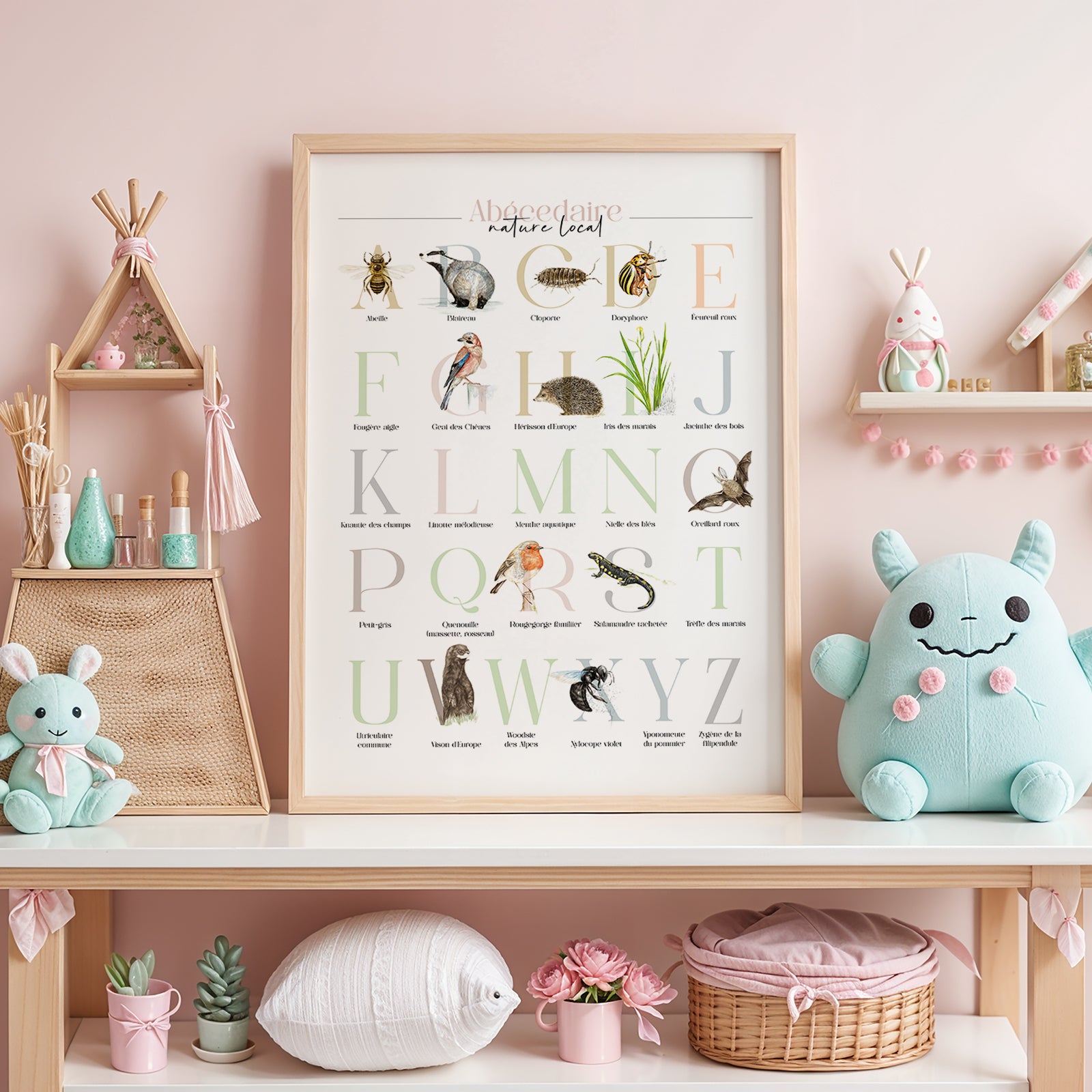Illustration encadrée de l’abécédaire de la faune et de la flore, posée sur une étagère dans une chambre d’enfant, avec un fond rose pastel.