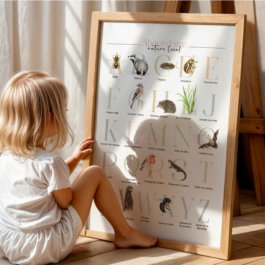 Affiche de l’abécédaire de la faune et de la flore posée au sol, observée avec curiosité par un enfant, découvrant la richesse de la biodiversité.